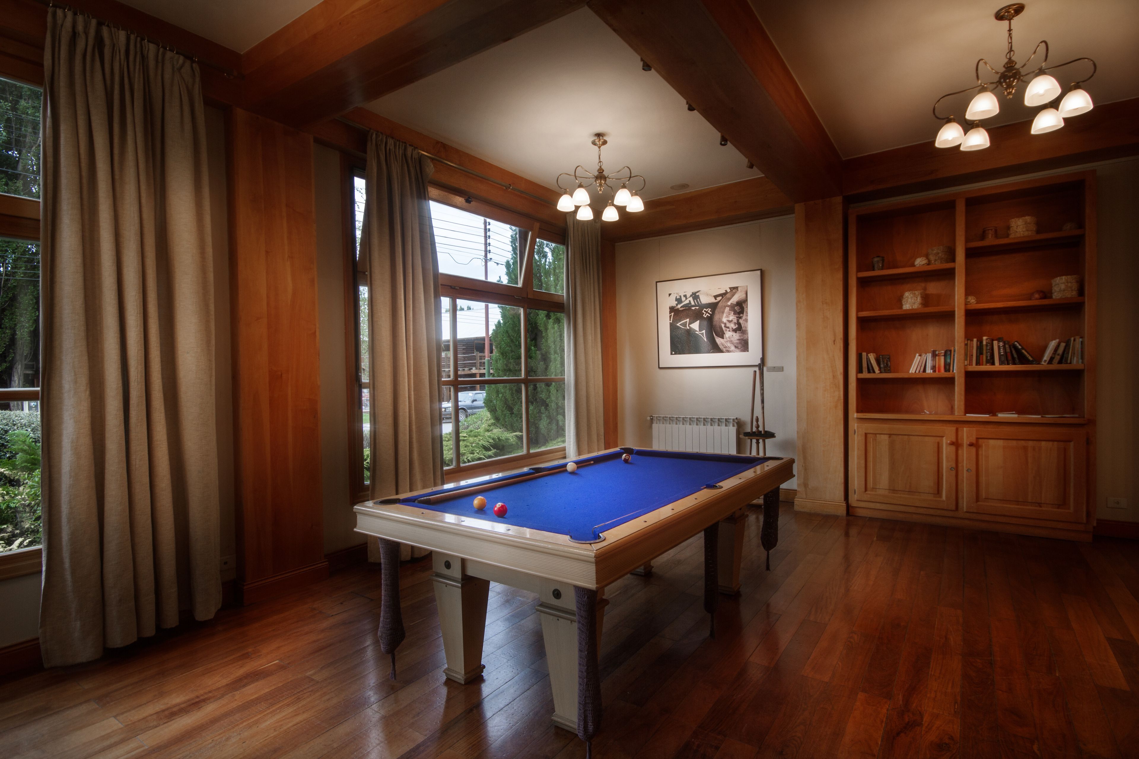 A pool table in a room with wooden floors and a large window.