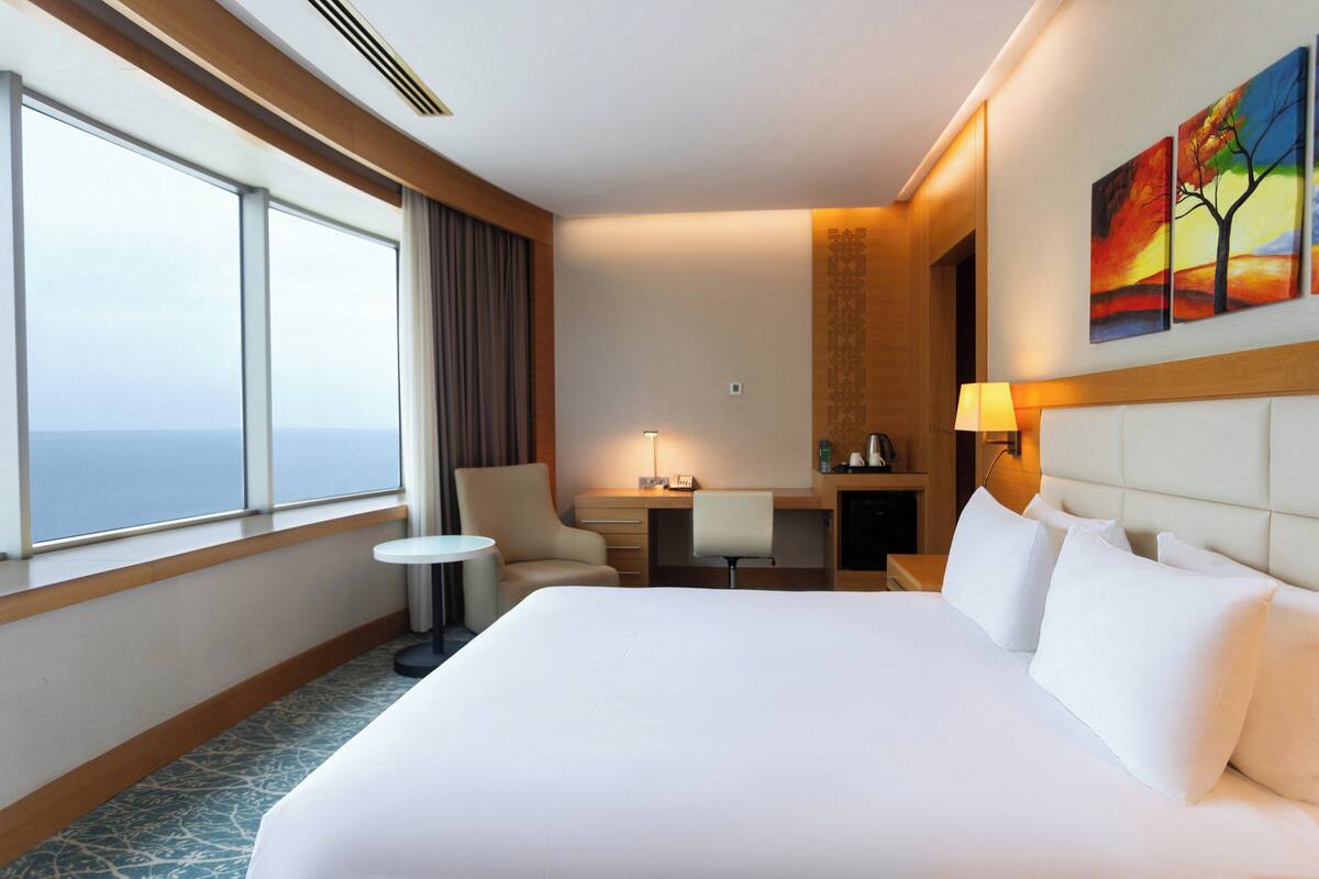 Habitación de hotel con una cama grande, un escritorio, una silla, una mesita y vista al océano.