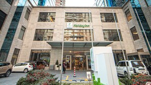 A Holiday Inn hotel with a modern glass facade, a central entrance, and a landscaped area with shrubs and a sign. - Holiday Inn Baku by IHG (Baku)