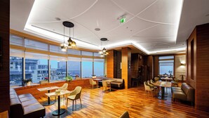 A modern hotel lobby with wooden flooring, seating areas, and large windows offering city views. - Holiday Inn Baku by IHG (Baku)