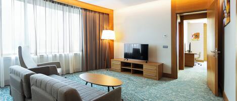 A hotel room with a sofa, a TV, a lamp, and a desk.