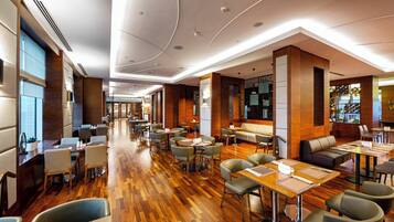 A spacious hotel lobby with multiple seating areas, including tables and chairs, and a central seating area with a sofa.