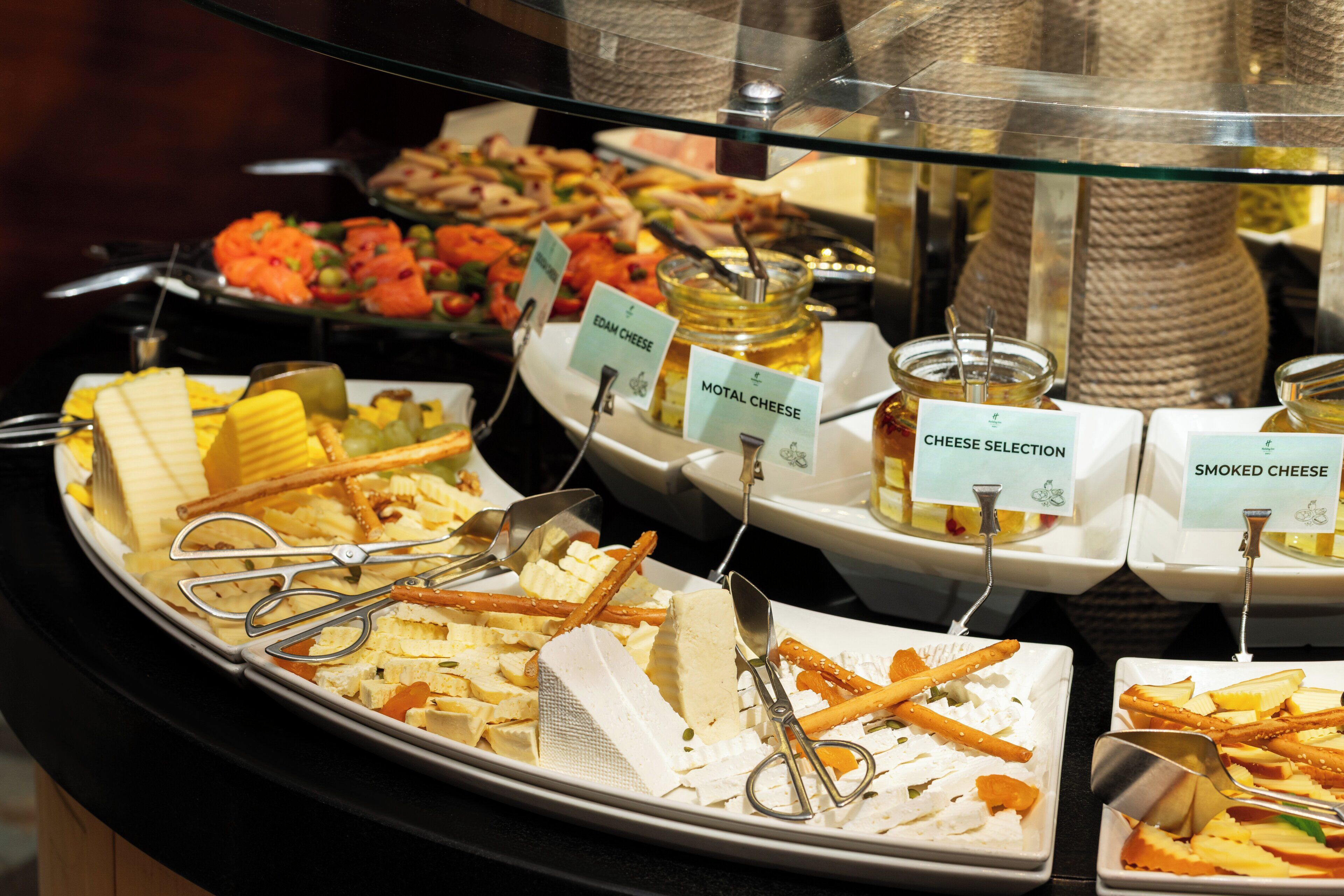 Un buffet proposant une variété de fromages, notamment de l’edam, du motar et du fromage fumé, ainsi que des couverts.