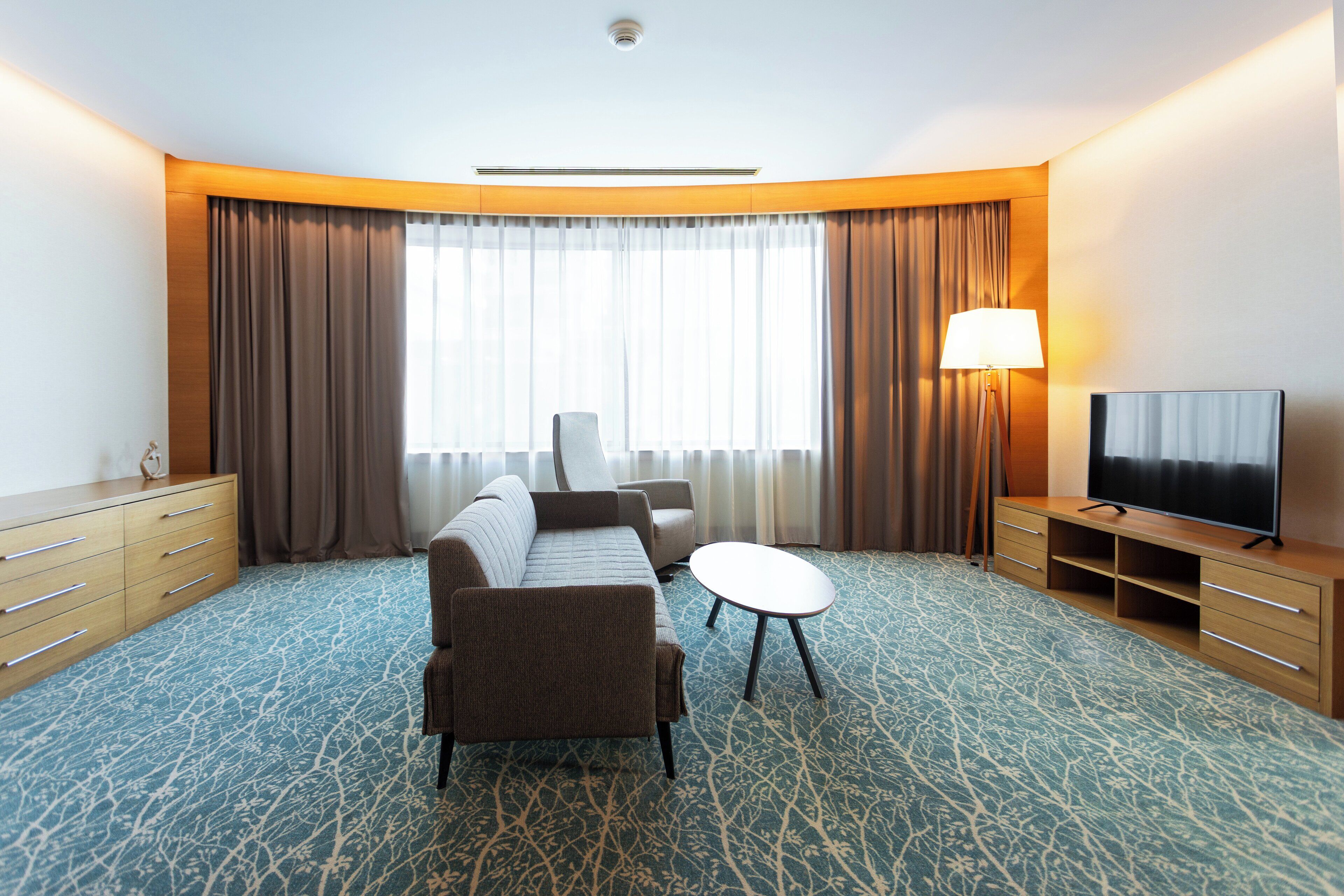 A hotel room with a sofa, a small round table, a TV, and a lamp.