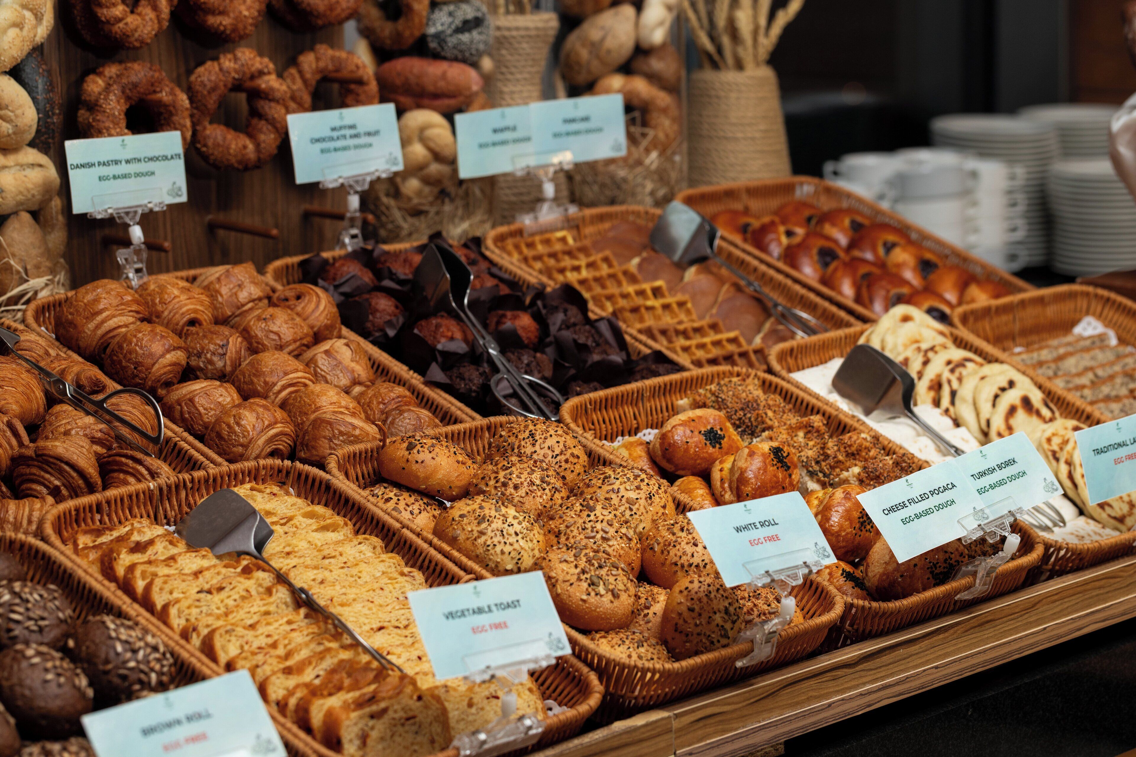 A bakery display with various baked goods like croissants, bread, and pastries, each labeled with their type and price.