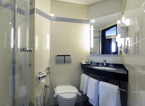 A modern bathroom with a glass shower enclosure, a toilet, a sink with a black countertop, and a mirror above the sink. - Ibis Seef Manama (Manama)