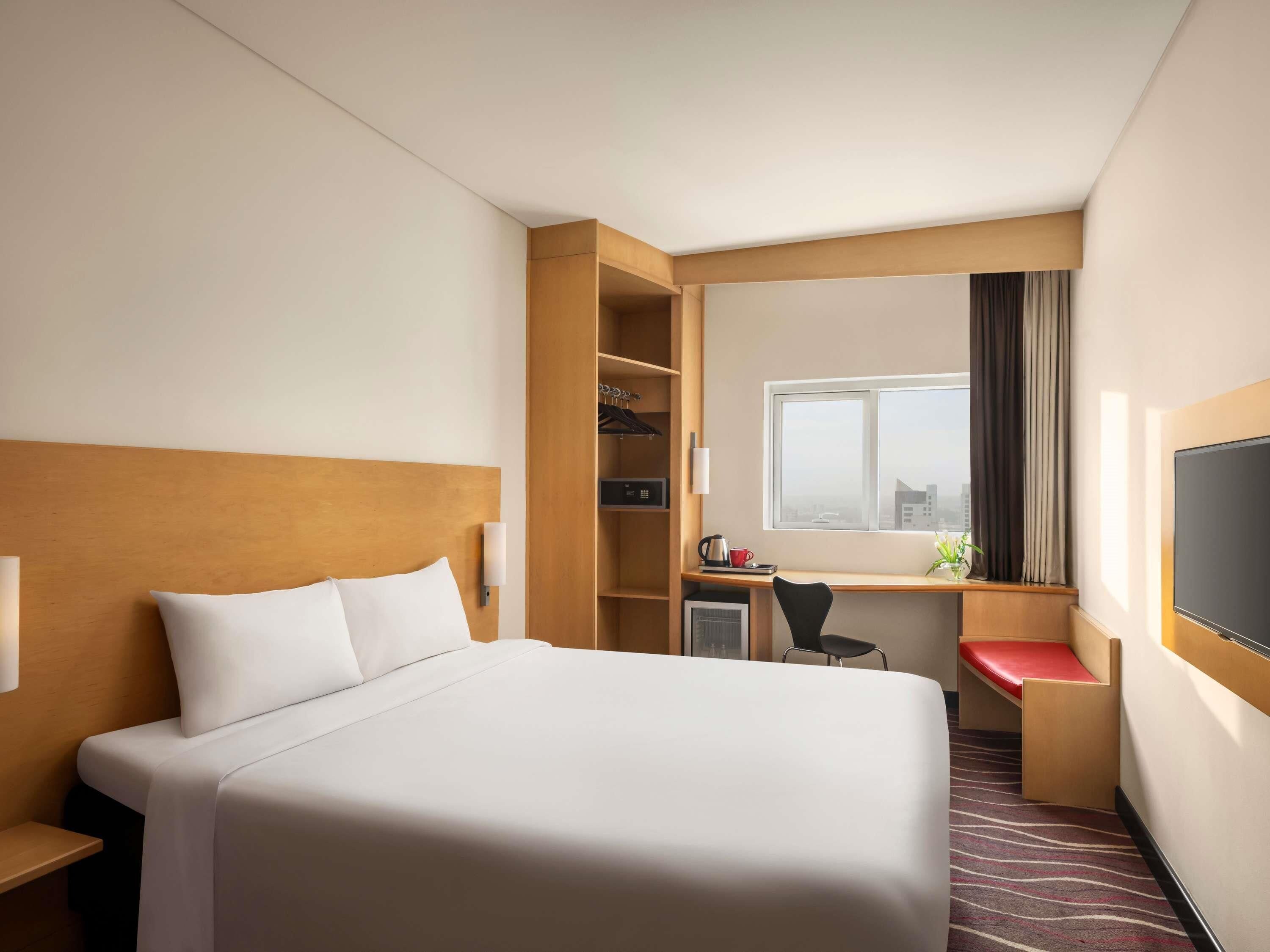 A hotel room with a large bed, a desk, a chair, a TV, and a window with curtains.