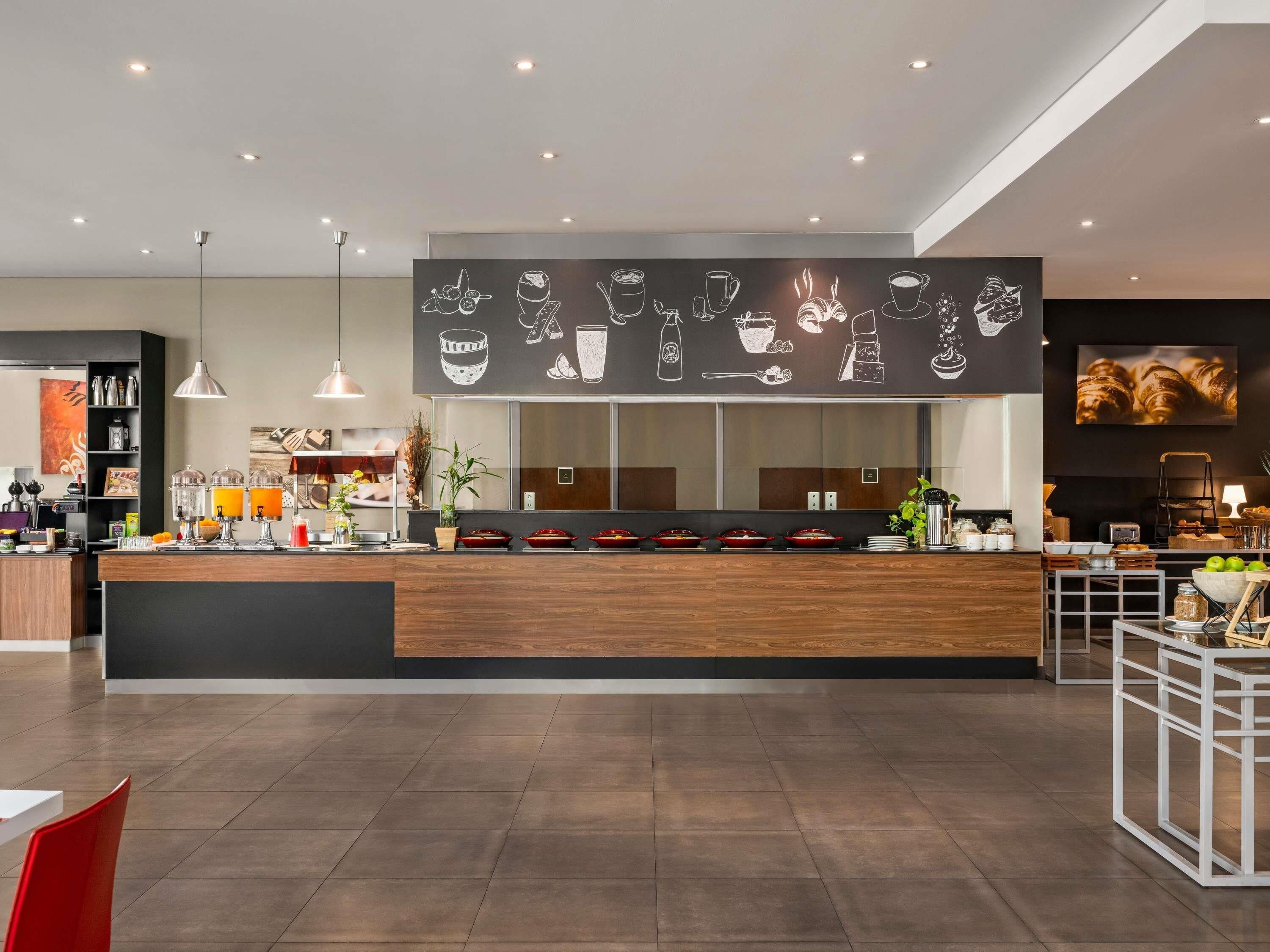 A modern cafe with a wooden counter, a wall mural of food and drink, and a clean, tiled floor.