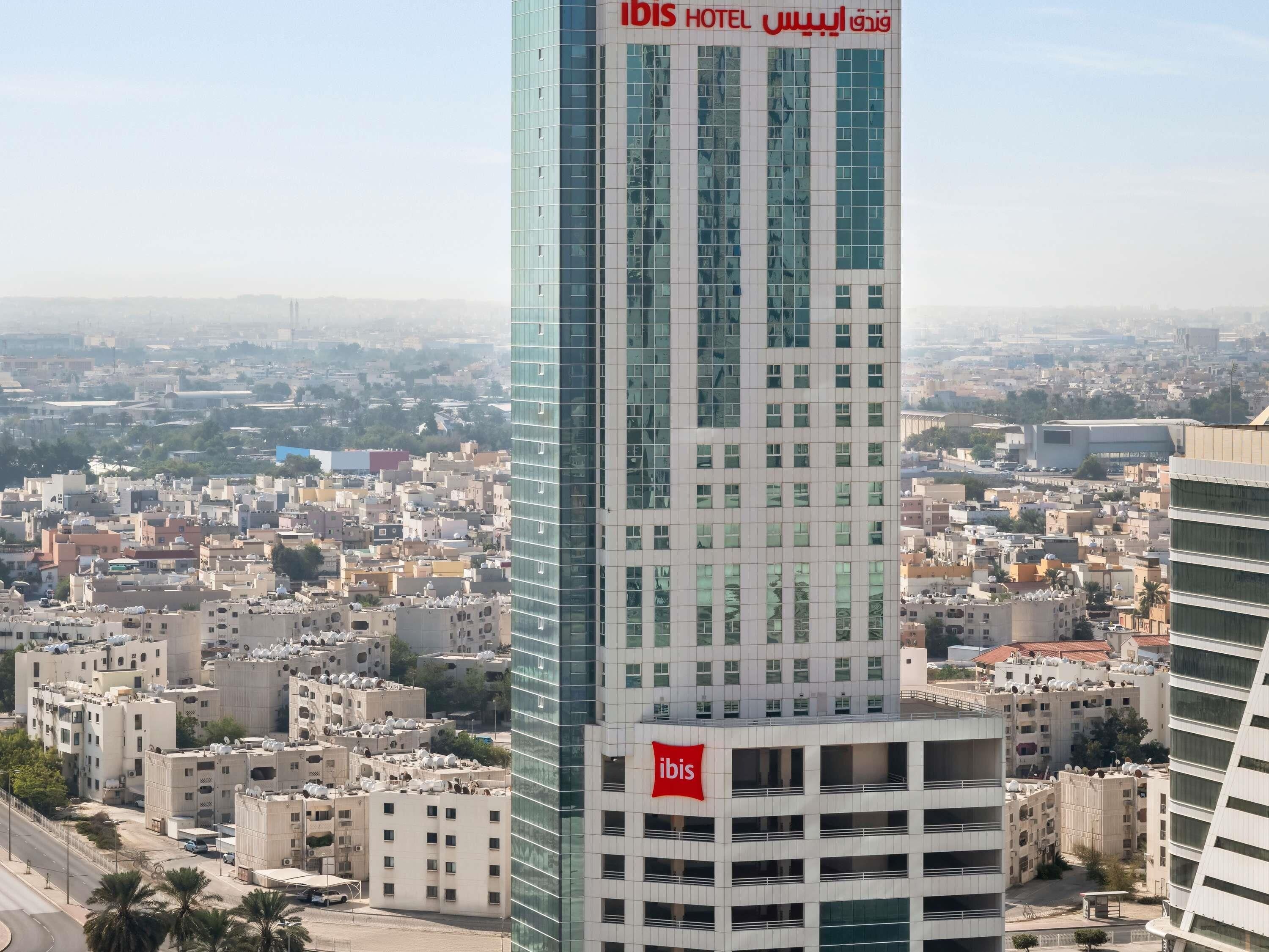 A high-rise hotel with a modern glass facade, multiple floors, and a prominent red logo.