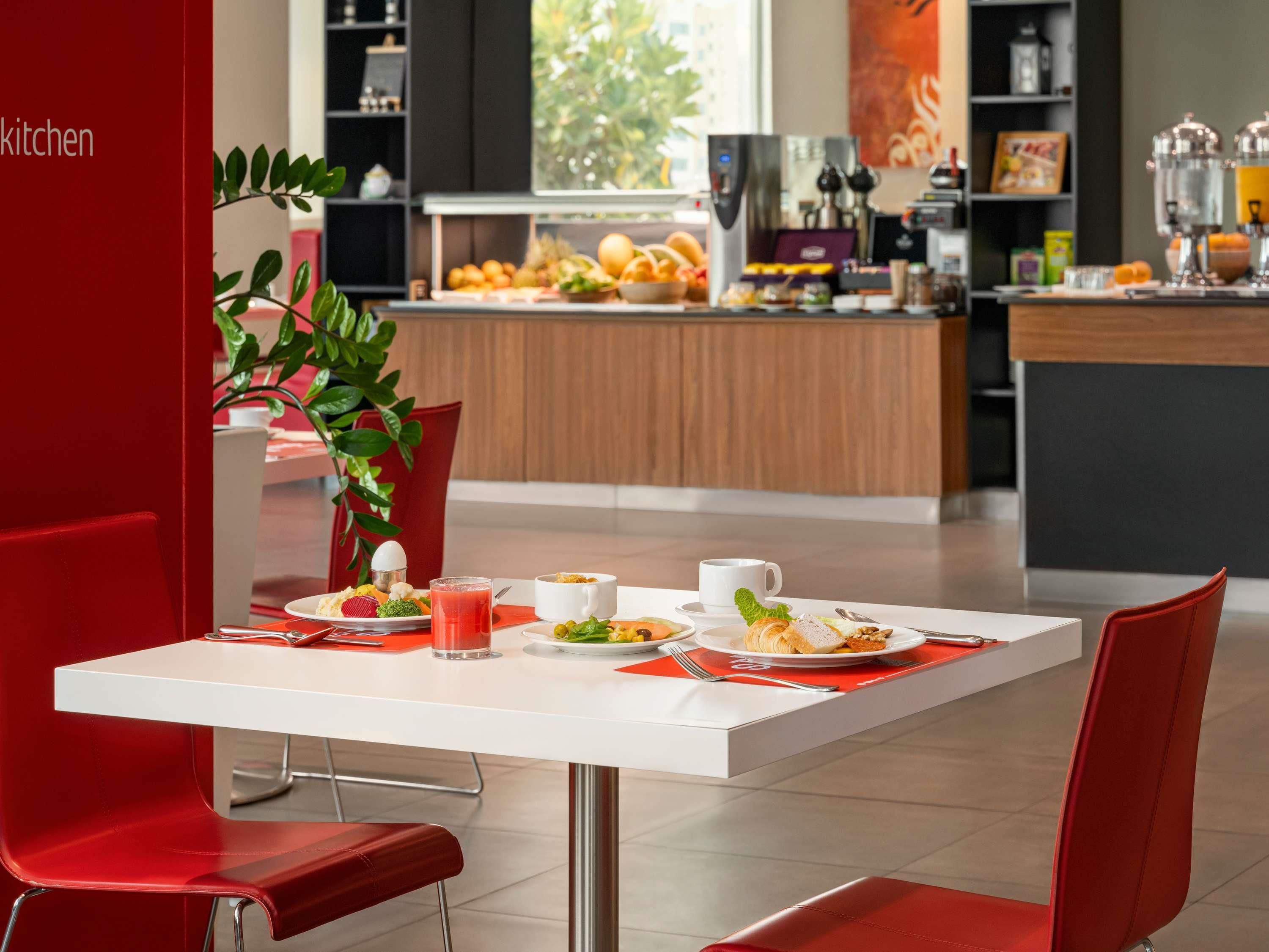 Un comedor moderno con una mesa blanca y sillas rojas, una cocina al fondo y vistas al exterior.