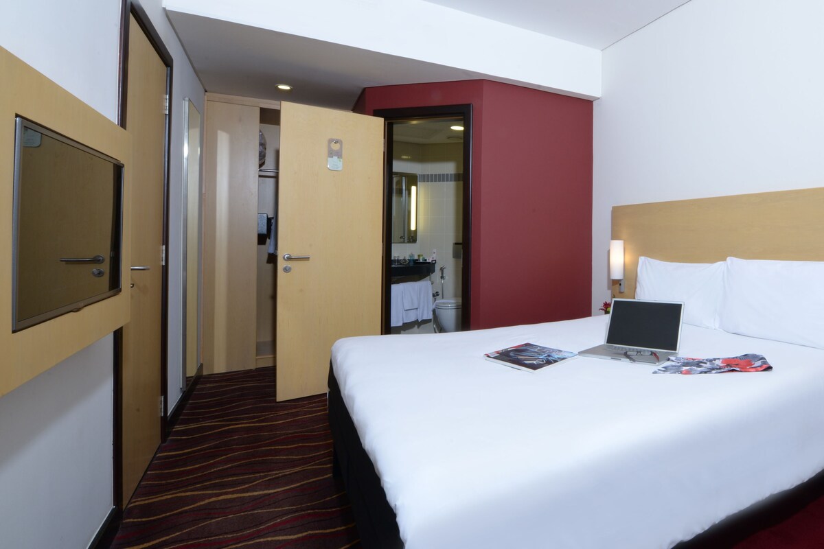 A hotel room with a bed, a laptop, a remote control, and a magazine on the bed.
