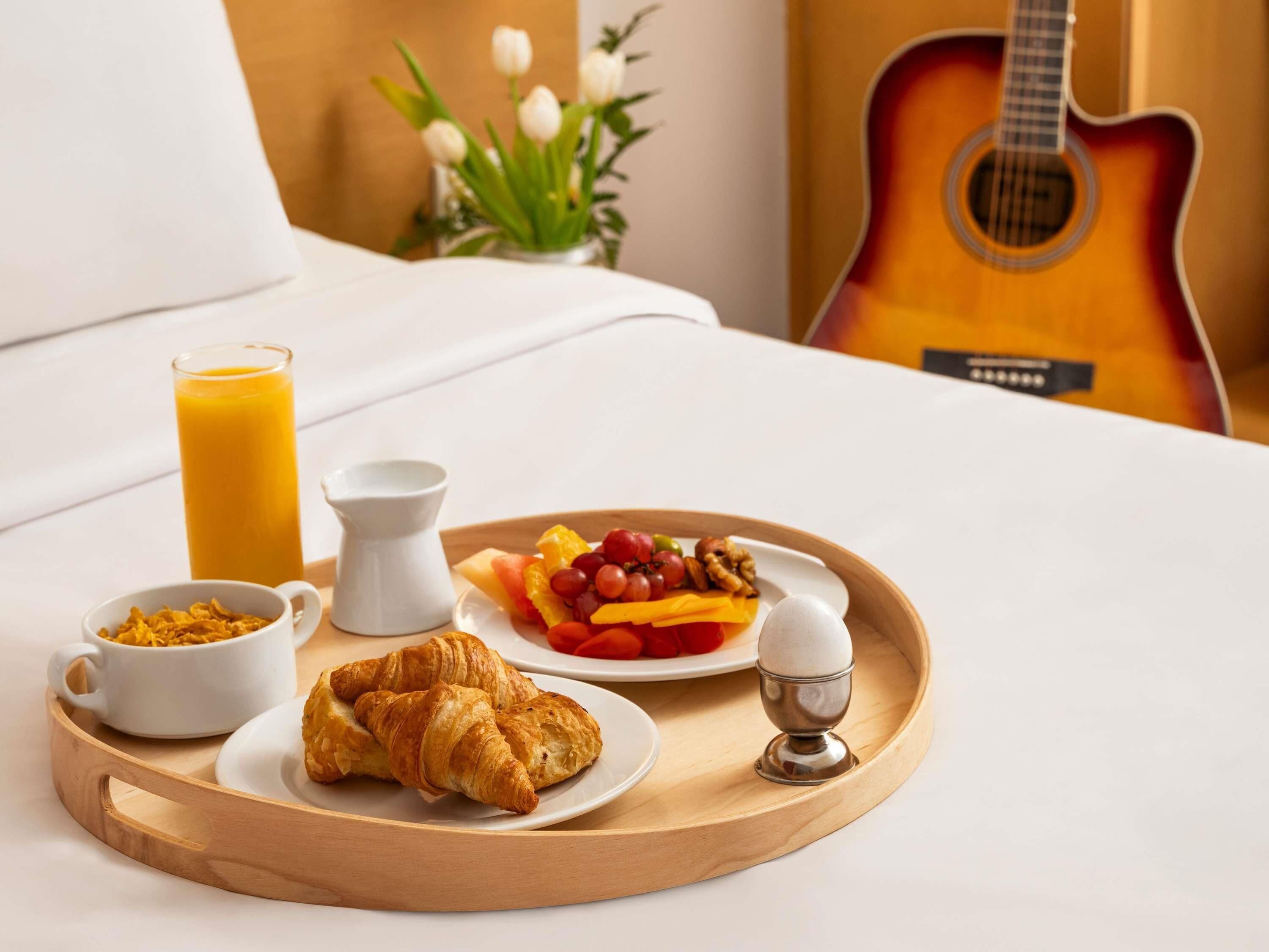 A breakfast tray with croissants, cereal, fruit, and a glass of orange juice on a bed.