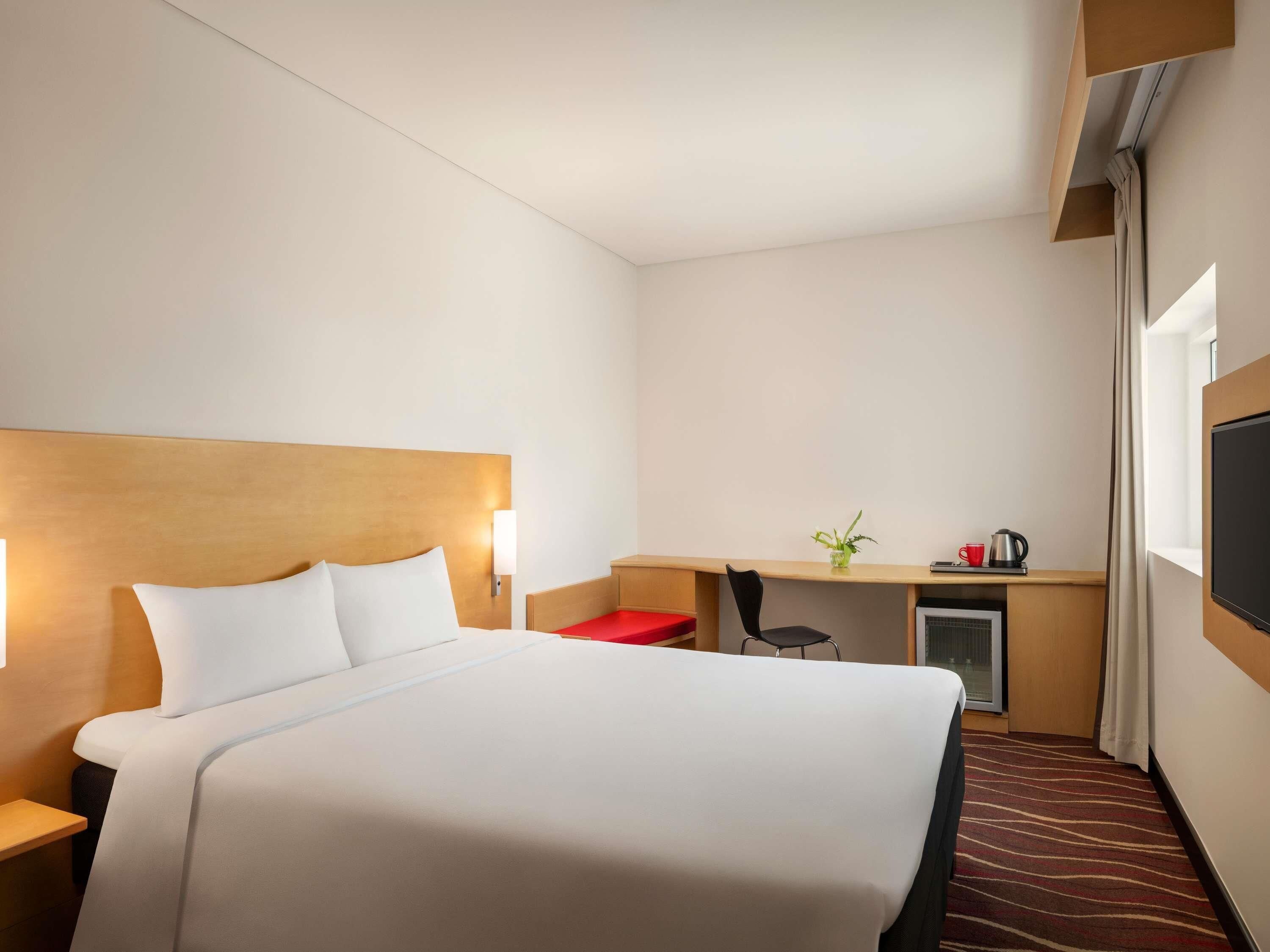 Une chambre d’hôtel comprenant un lit, un bureau, une chaise, une petite table, un téléviseur et une fenêtre.