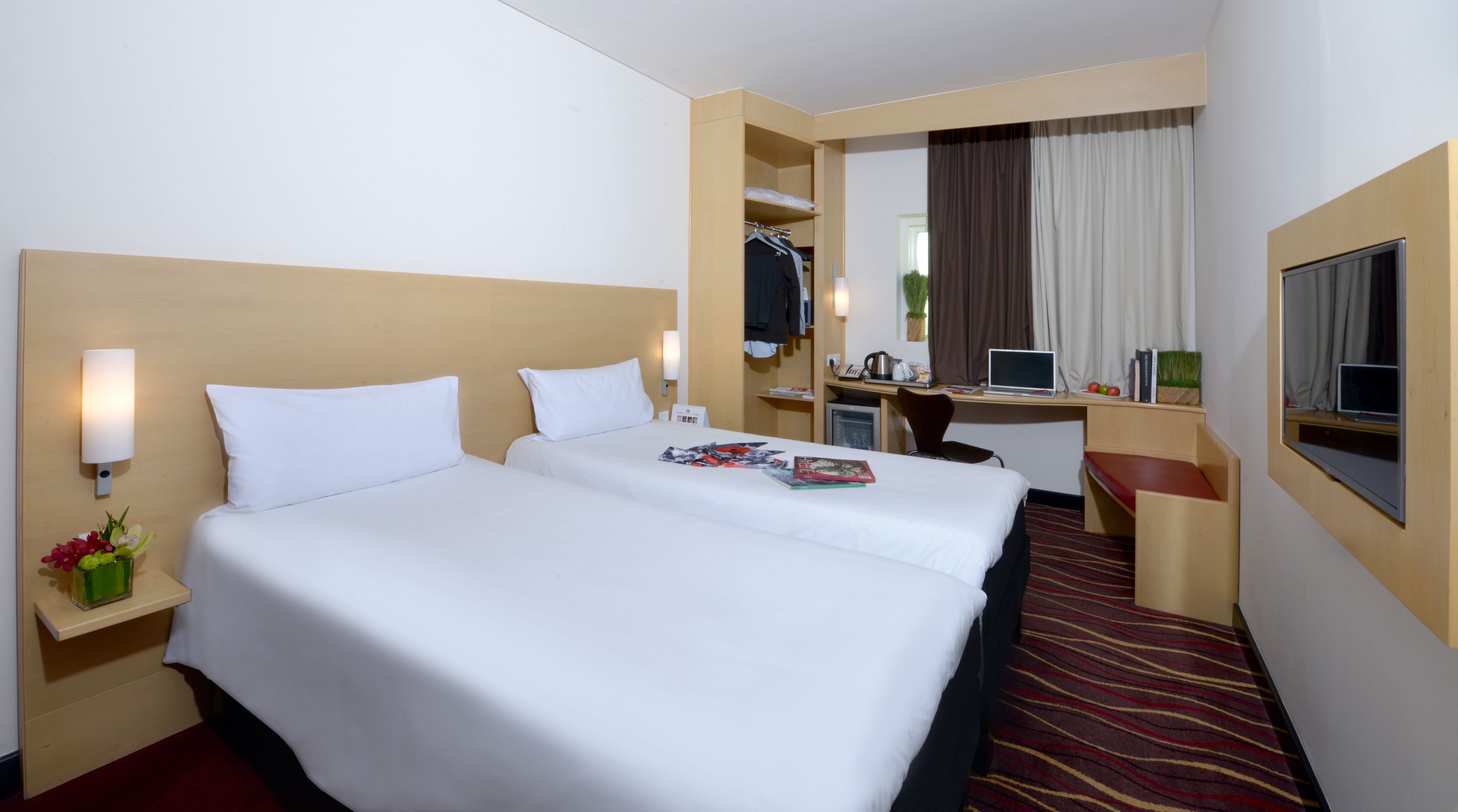 Een hotelkamer met een groot bed, een bureau met een laptop, een spiegel en een televisie.