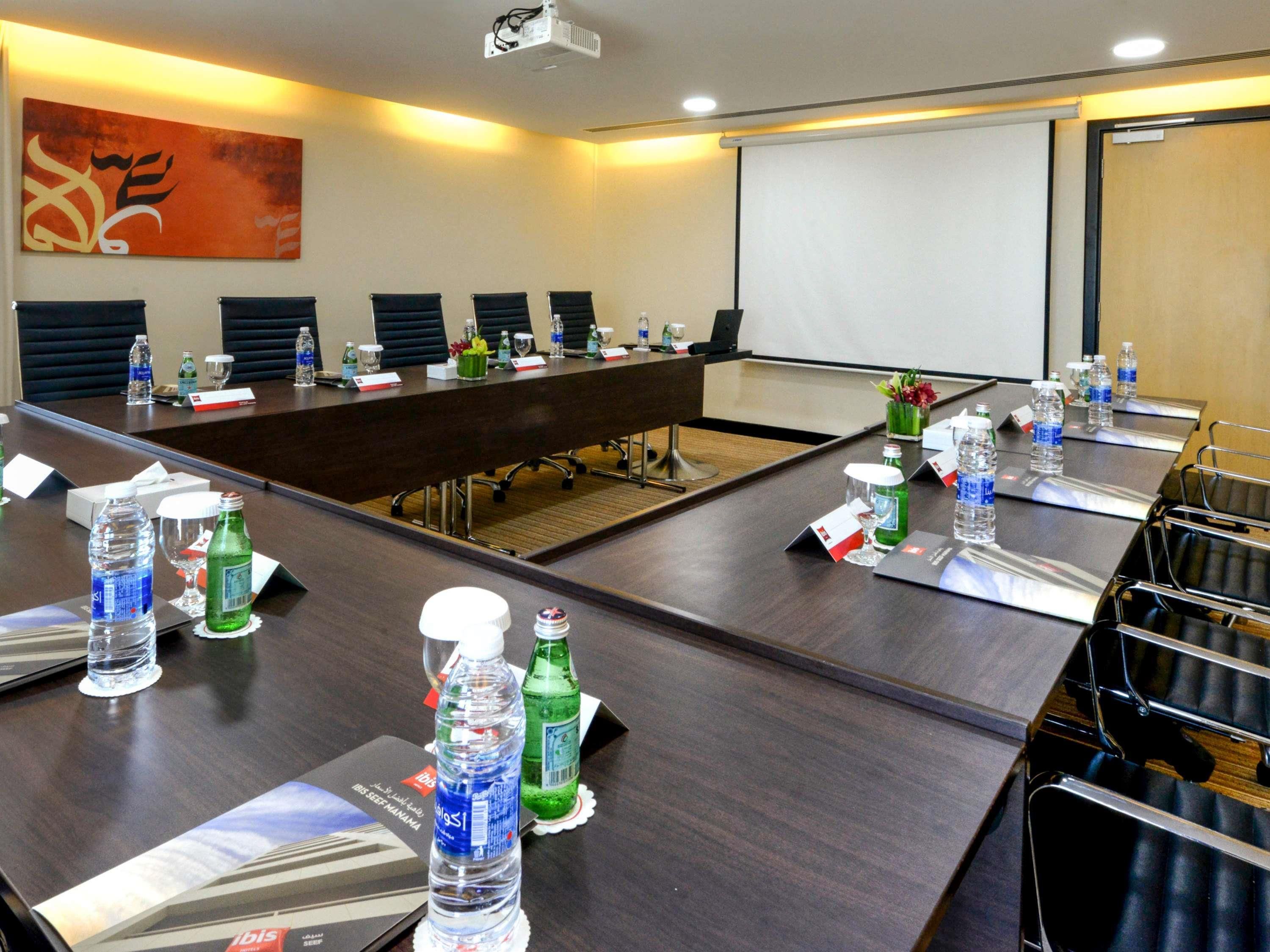 A conference room with a long table, chairs, water bottles, and a projector screen.