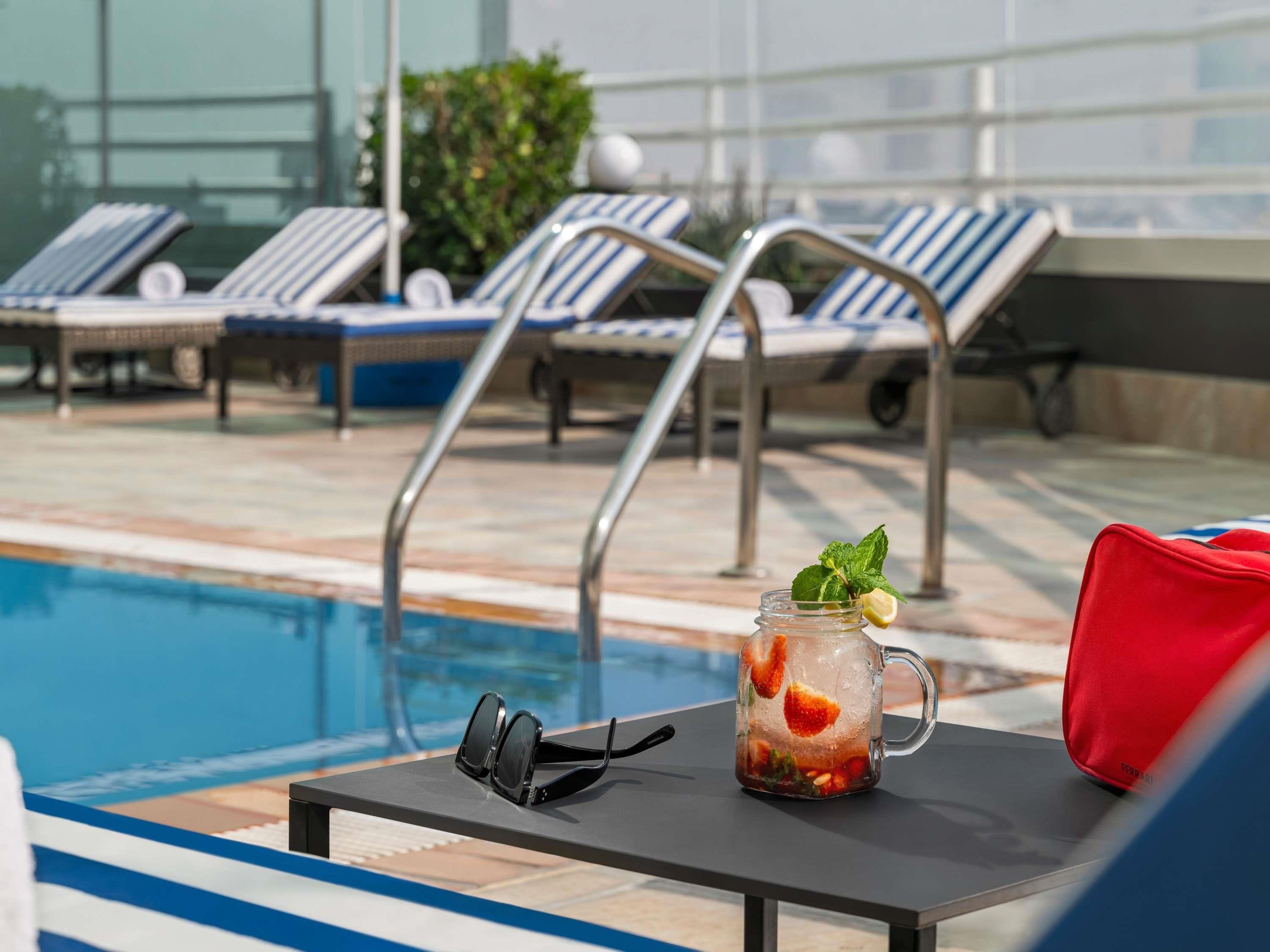 Zona de piscina con sillas de descanso, una mesa con una bebida y gafas de sol.