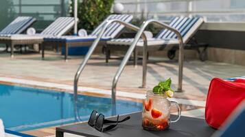 Zona de piscina con sillas de descanso, una mesa con una bebida y gafas de sol.