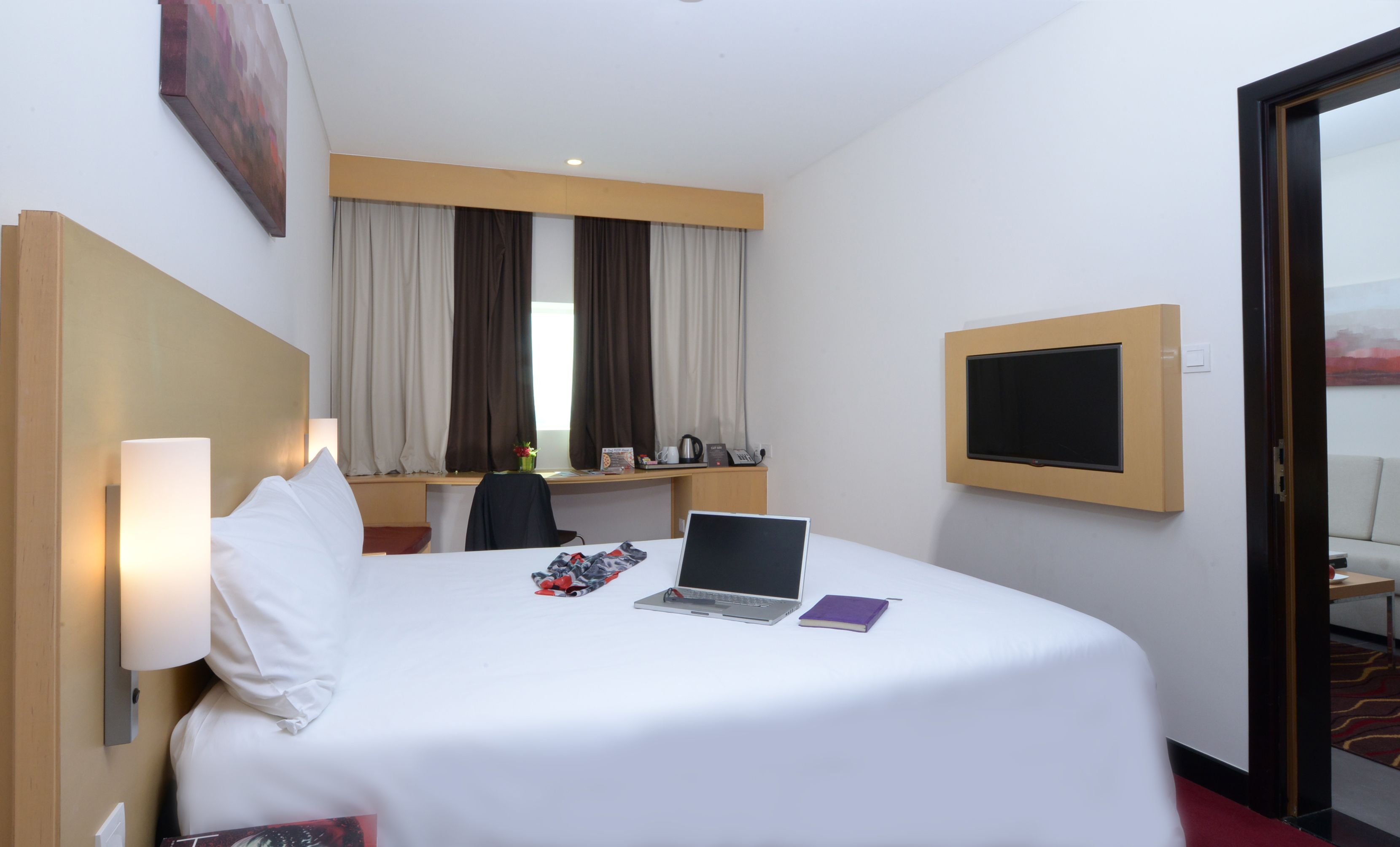 A hotel room with a bed, a desk, a laptop, and a TV.