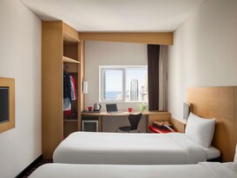 Una habitación de hotel con dos camas, un escritorio con una computadora portátil, una silla y vistas a la ciudad.