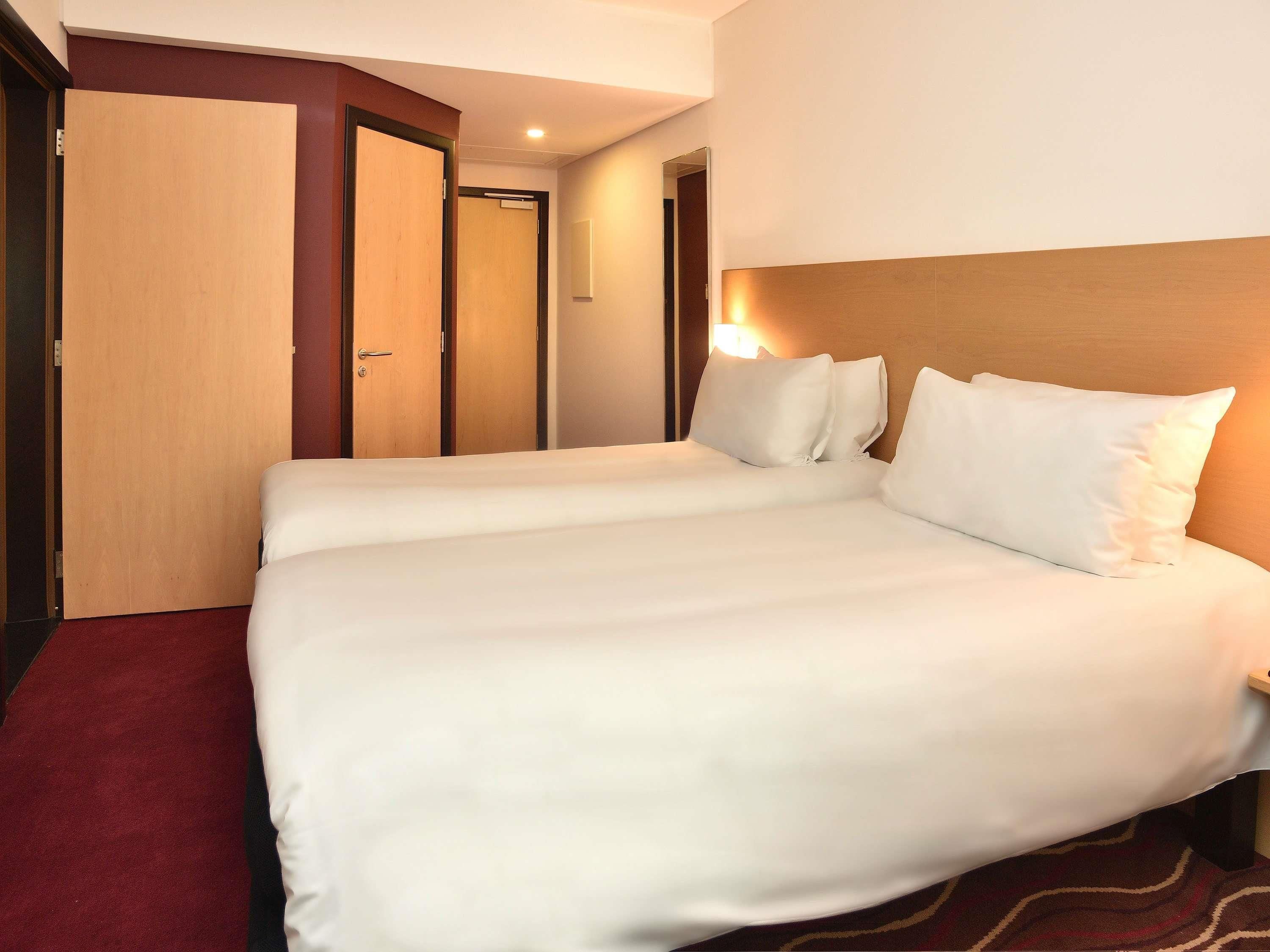 Una habitación de hotel con una cama grande, dos puertas, un cabecero y suelo alfombrado.