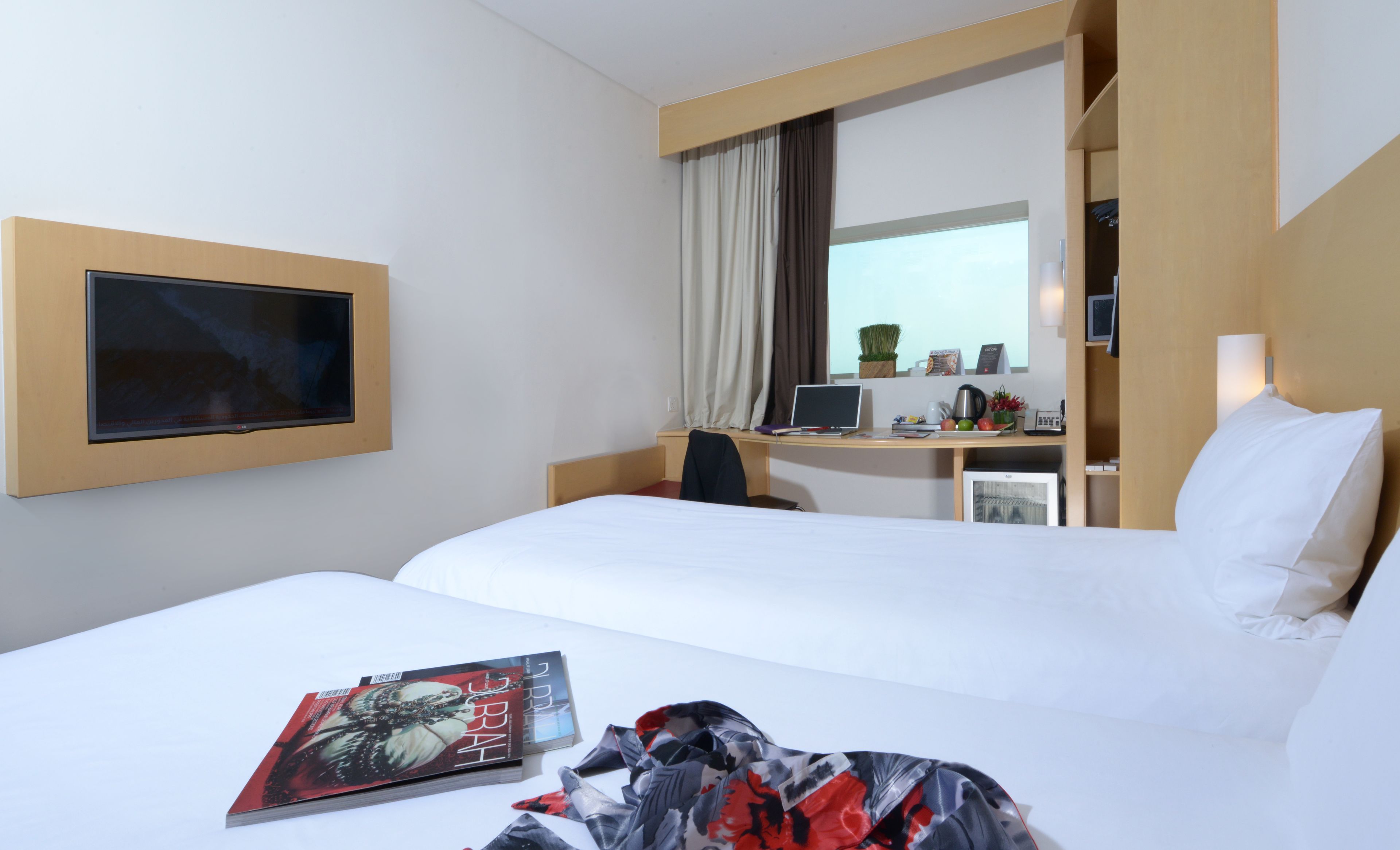 A hotel room with a bed, a desk with a computer, a TV, and a window with curtains.