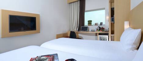A hotel room with a bed, a desk with a computer, a TV, and a window with curtains.