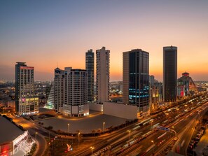 A cityscape with modern high-rise buildings, including a prominent hotel with a lit sign. - Ibis Seef Manama (Manama)