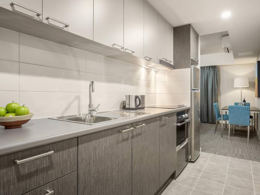 Una cocina moderna con armarios grises, un lavamanos de acero inoxidable y un hervidor. Hay un bol con manzanas verdes en la encimera.