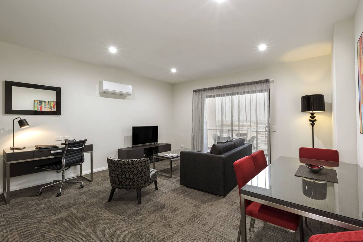A modern hotel room with a desk, chair, sofa, and a dining table with chairs.