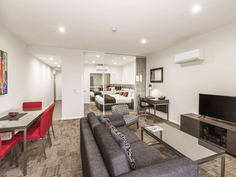A modern living room with a sofa, red chairs, a glass coffee table, a flat-screen TV, and a dining area with a table and chairs.
