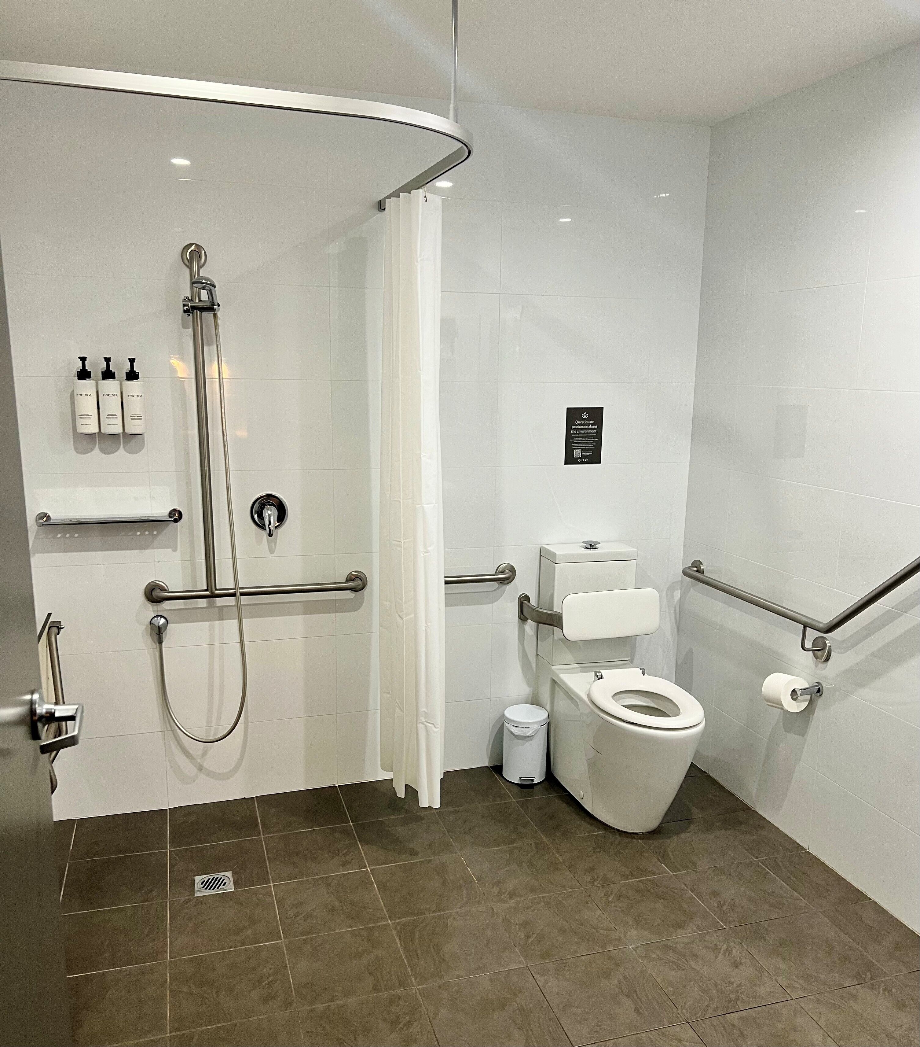 A modern bathroom with a shower, toilet, and handrails.