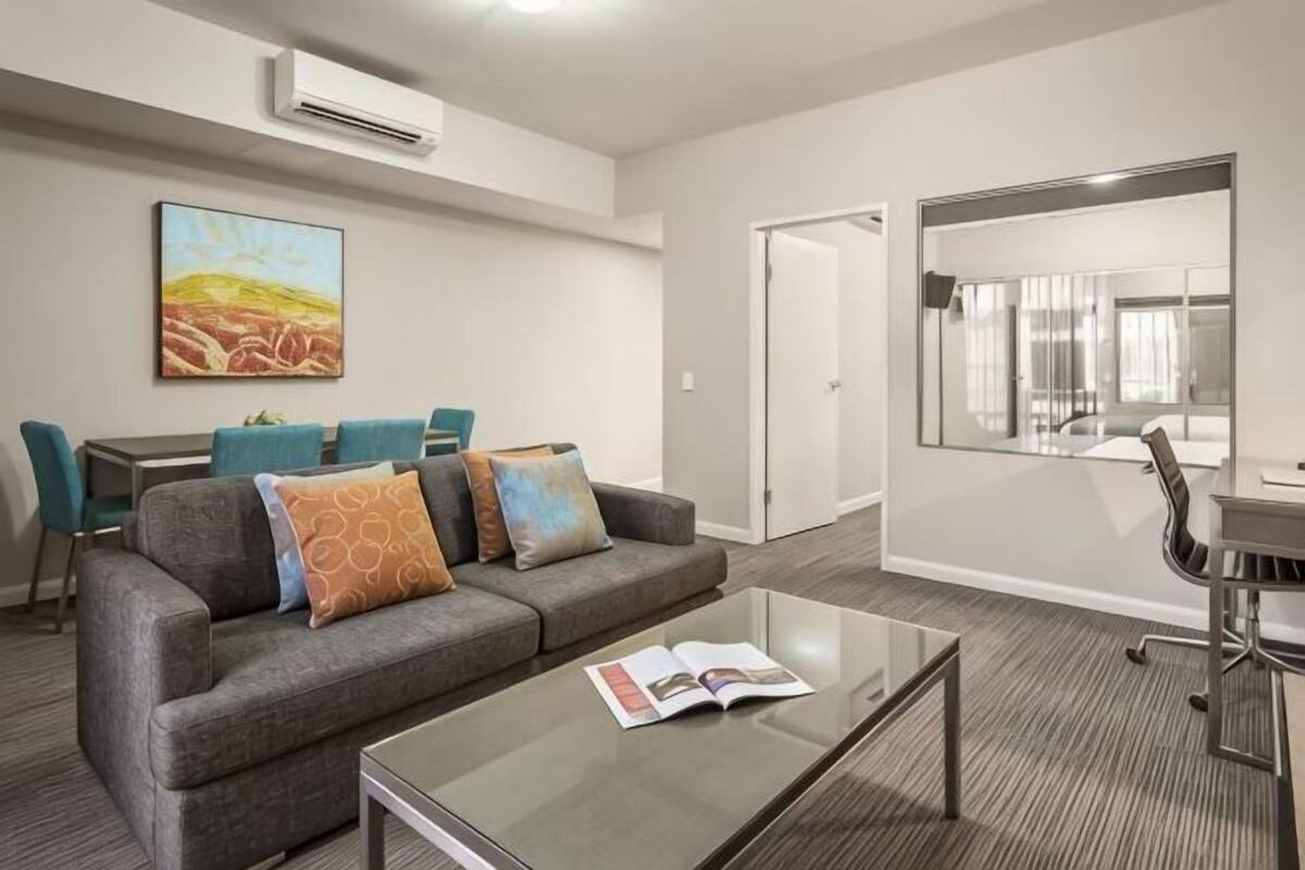 A modern room with a gray sofa, a glass coffee table, a dining area with chairs, and a large mirror.