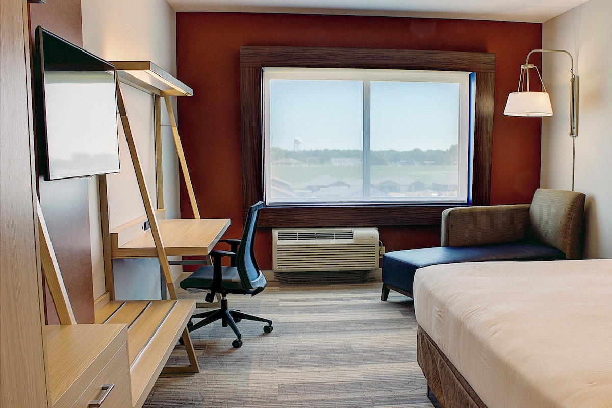 A hotel room with a bed, desk, chair, and a window with a view.