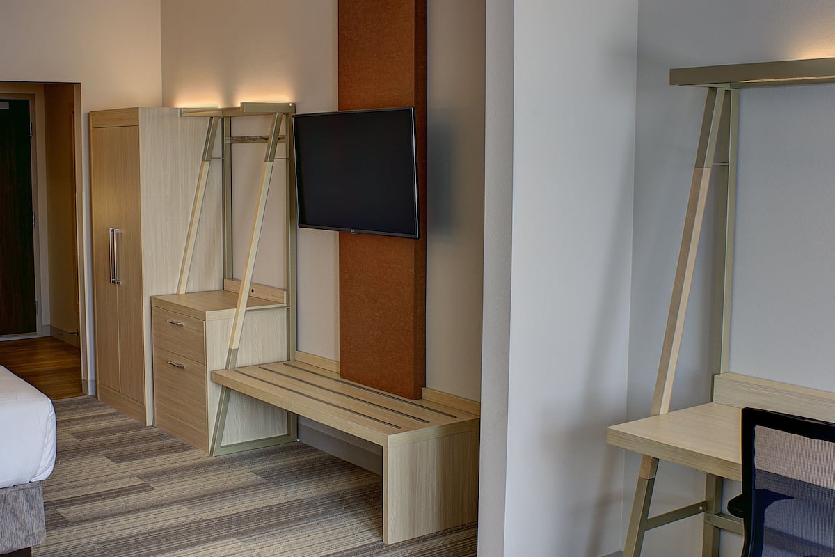 A hotel room with a bed, a desk, a chair, a TV mounted on the wall, and a wardrobe.