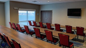 Un salón de conferencias con una larga mesa y sillas rojas, una puerta y un televisor en la pared.