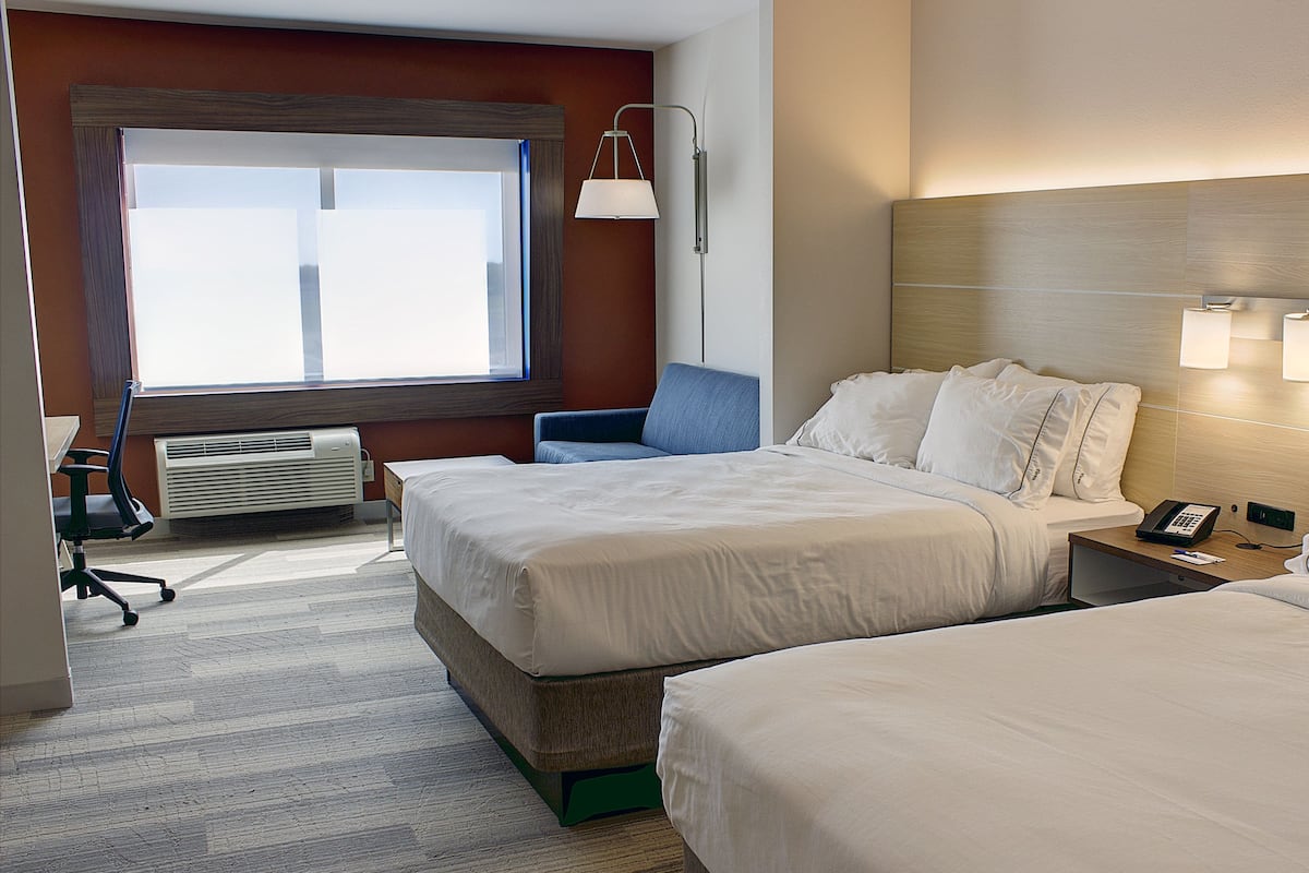 A hotel room with two beds, a desk, a chair, a lamp, and a window.