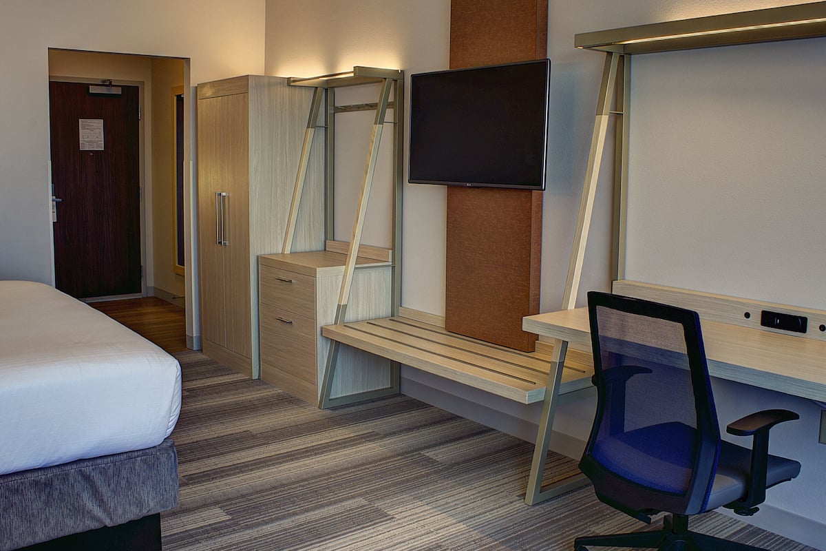 A hotel room with a bed, a desk with a chair, a television, and a wardrobe.