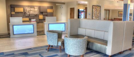 A hotel lobby with a reception desk, seating area, and a refrigerator.