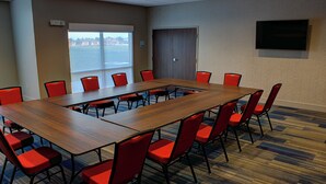 A conference room with a long table and red chairs, a door, and a TV on the wall.