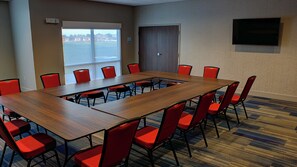 Une salle de conférence avec une longue table et des chaises rouges, une porte et un téléviseur fixé au mur.