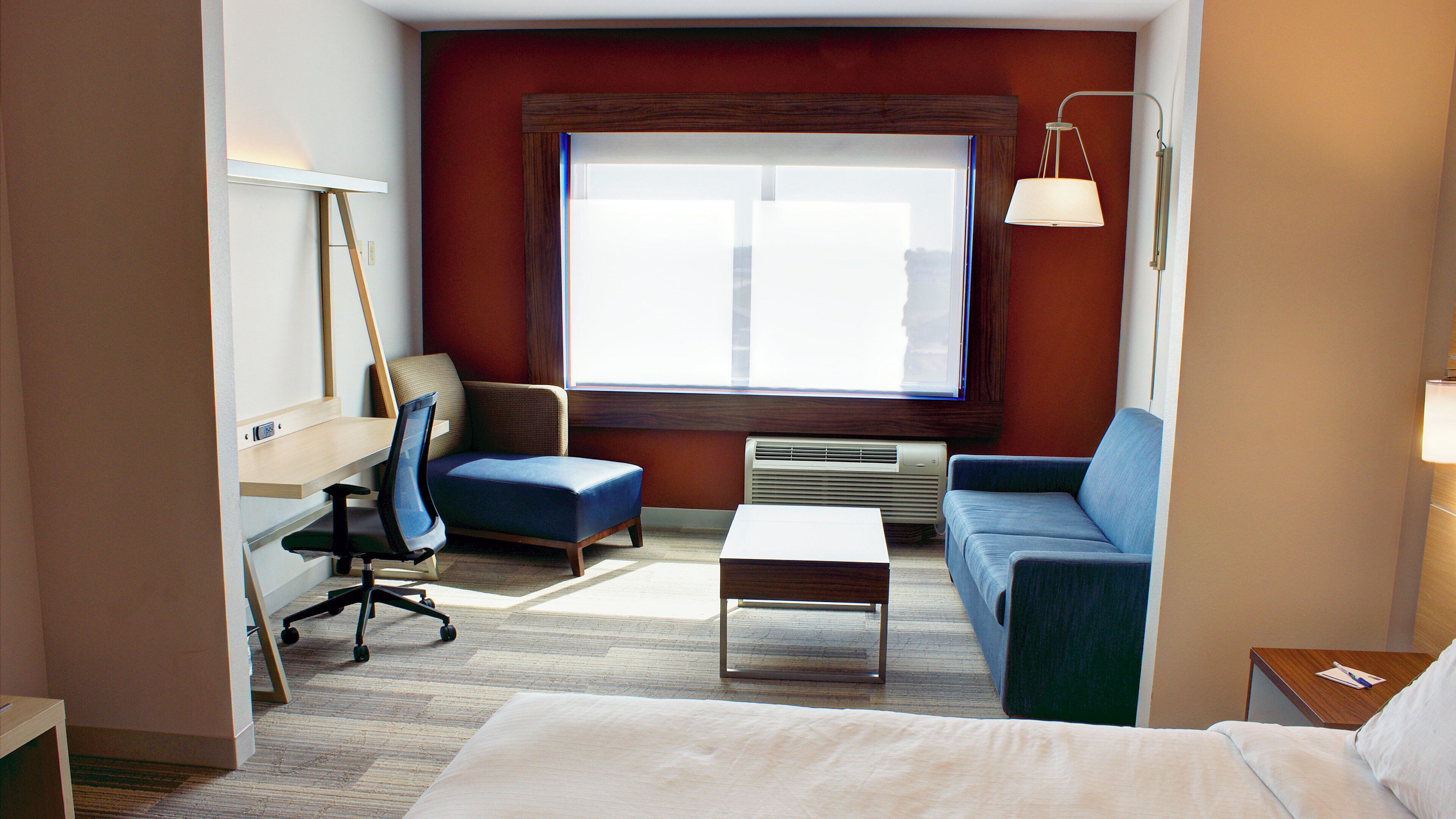 A hotel room with a bed, a desk, a chair, a sofa, and a large window.