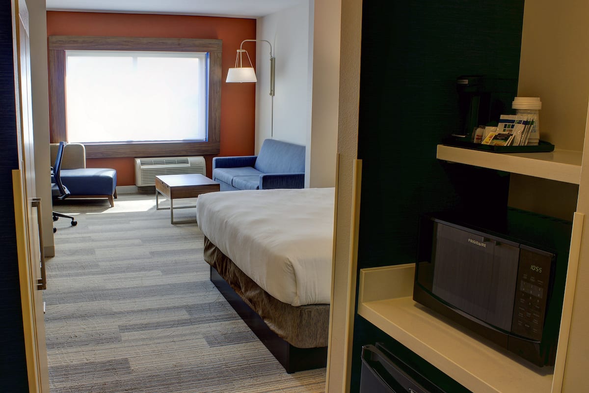 A hotel room with a bed, a desk, a chair, a sofa, a TV, and a window.