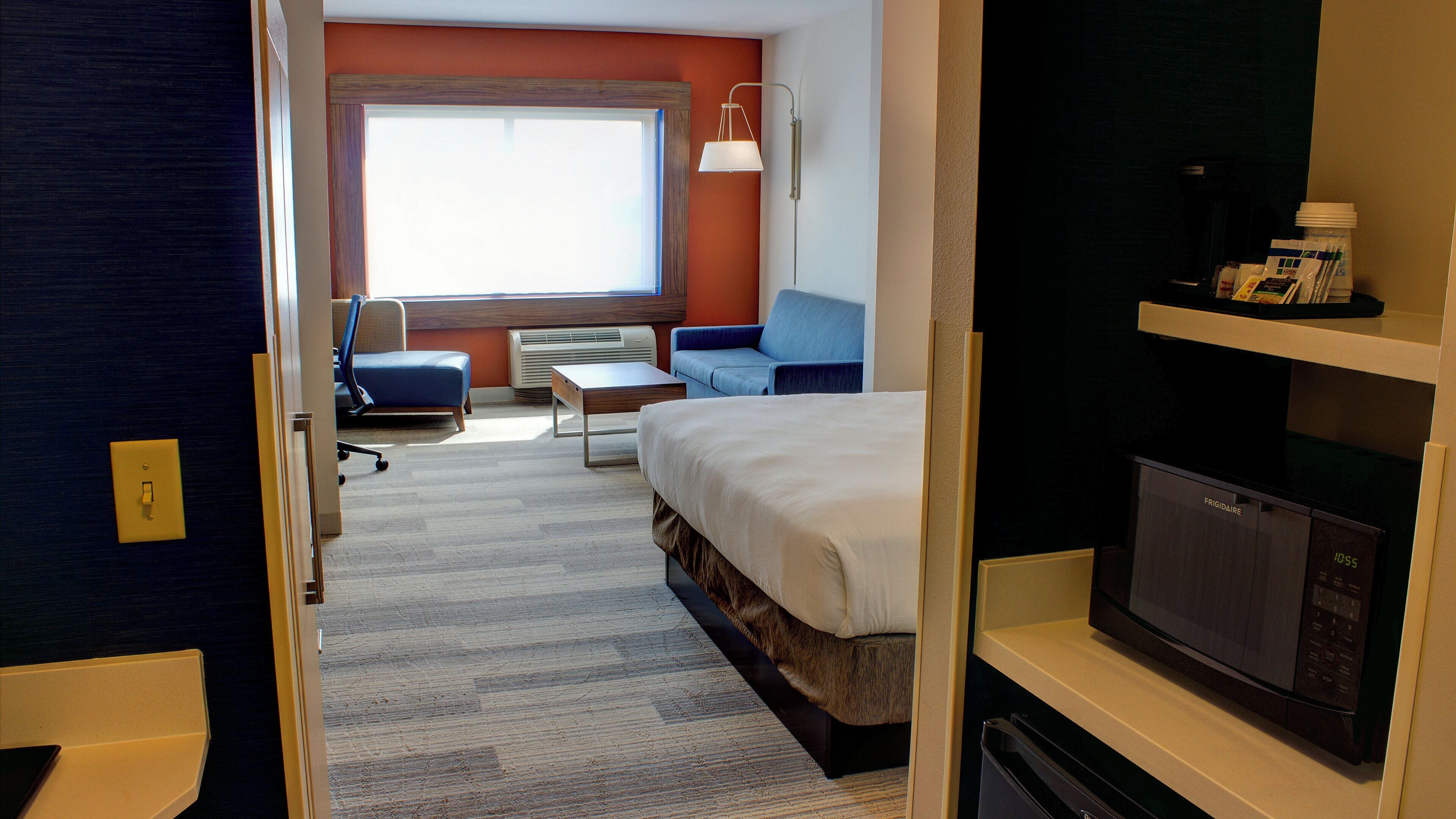 Ein Hotelzimmer mit Bett, Schreibtisch, Stuhl, Sofa, Mikrowelle und Fernseher.