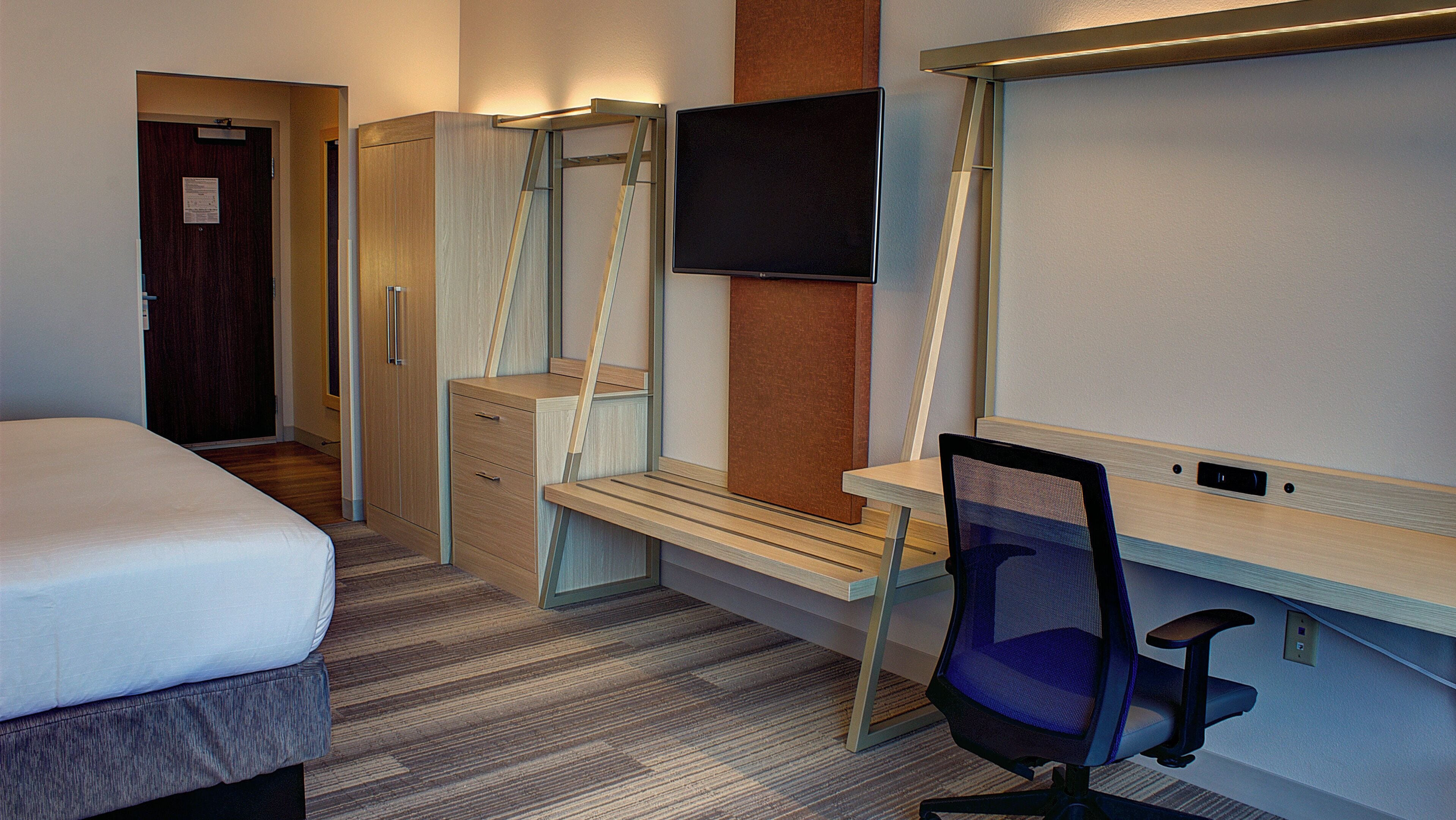 Una habitación de hotel con cama, escritorio, silla, televisor y armario.