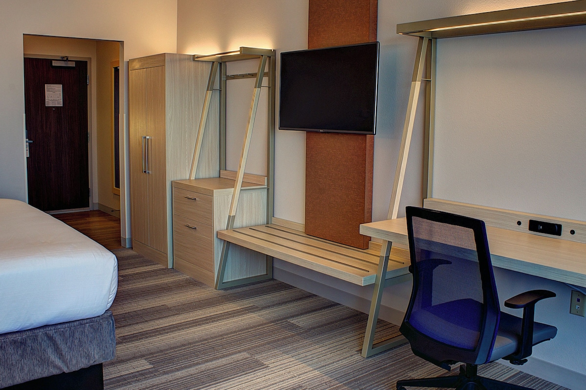 A hotel room with a bed, a desk, a chair, a TV, and a wardrobe.