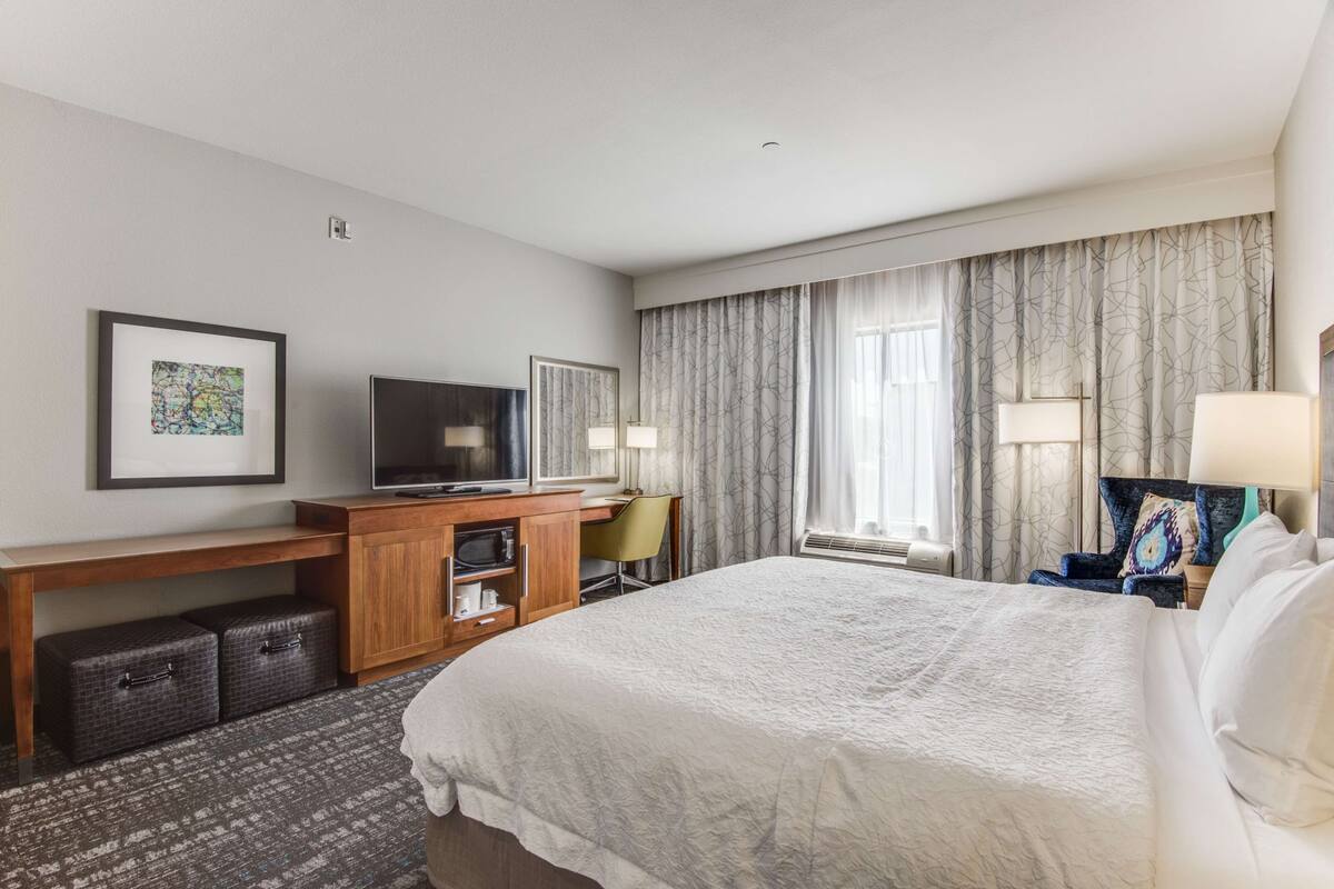 Une chambre d’hôtel avec un grand lit, un bureau avec une télévision, une chaise et un petit coin salon avec une lampe.
