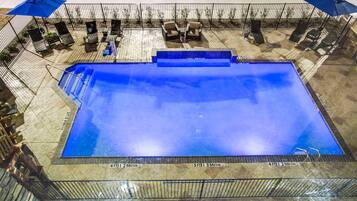 A rectangular swimming pool with a tiled deck surrounding it, equipped with lounge chairs and umbrellas.