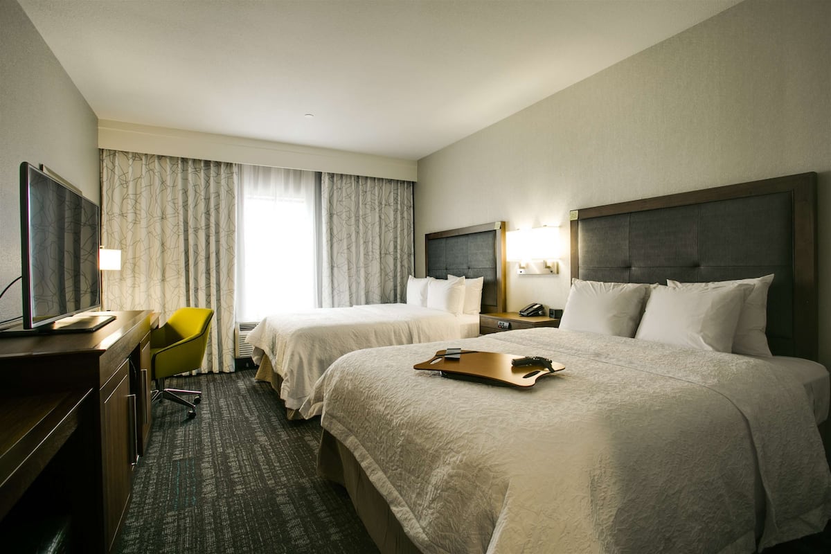 Une chambre d’hôtel avec deux lits, un bureau avec une chaise, une télévision et une fenêtre avec des rideaux.