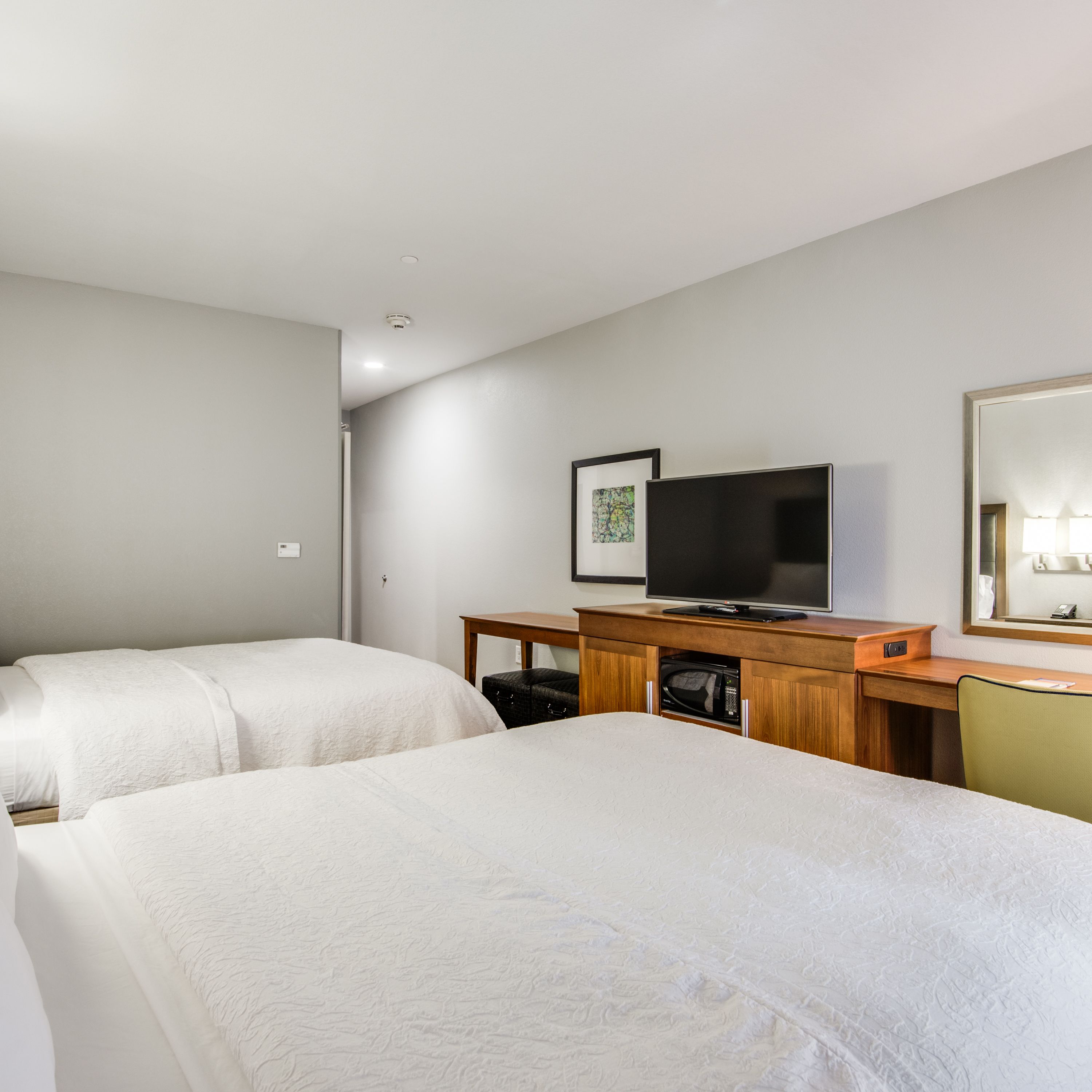 A hotel room with two beds, a television, a desk, and a microwave.