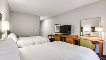 A hotel room with two beds, a desk with a television, and a mirror.